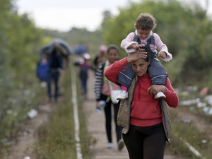 A migrant woman carries a child on her shoulders as they walk along railway tracks to cross the border between Serbia and Hungary, near Horgos, Serbia, Monday, Sept. 7, 2015. Frontex, the EU border agency, says more than 340,000 asylum seekers have entered the 28-nation bloc this year, the majority fleeing war and human rights abuses in Syria, Afghanistan, Iraq, Somalia and Eritrea. (AP Photo/Darko Vojinovic)